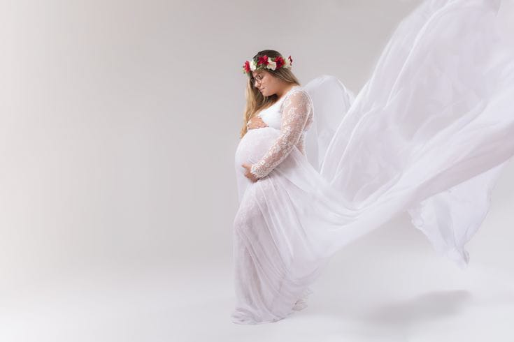 Future maman souriante en robe de grossesse fluide sur un fond blanc