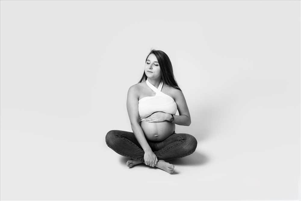 Photographie de future maman en noir et blanc en jean et crop top blanc sur fond blanc
