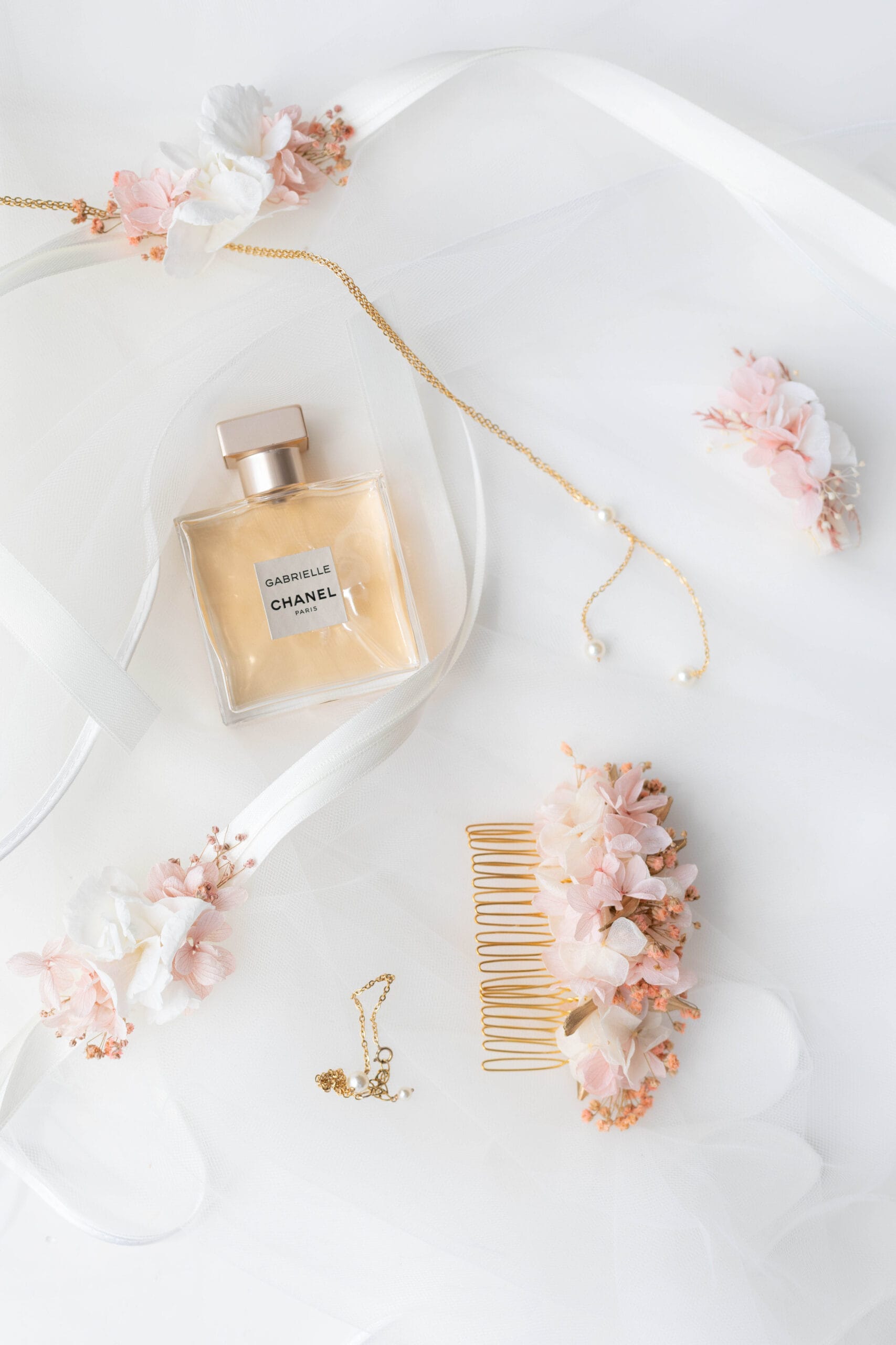 Parfum Gabrielle de Chanel et accessoires de la mariée posés sur un voile blanc.