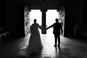 Silhouette en contre-jour des mariés à l'entrée de l'église, main dans la main.