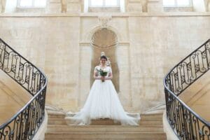 La mariée en robe longue pose dans le splendide escalier en pierre de l'abbaye aux dames de Caen