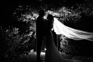 Magnifique photo de nuit des mariés en contre-jour avec le long voile qui vole au vent.