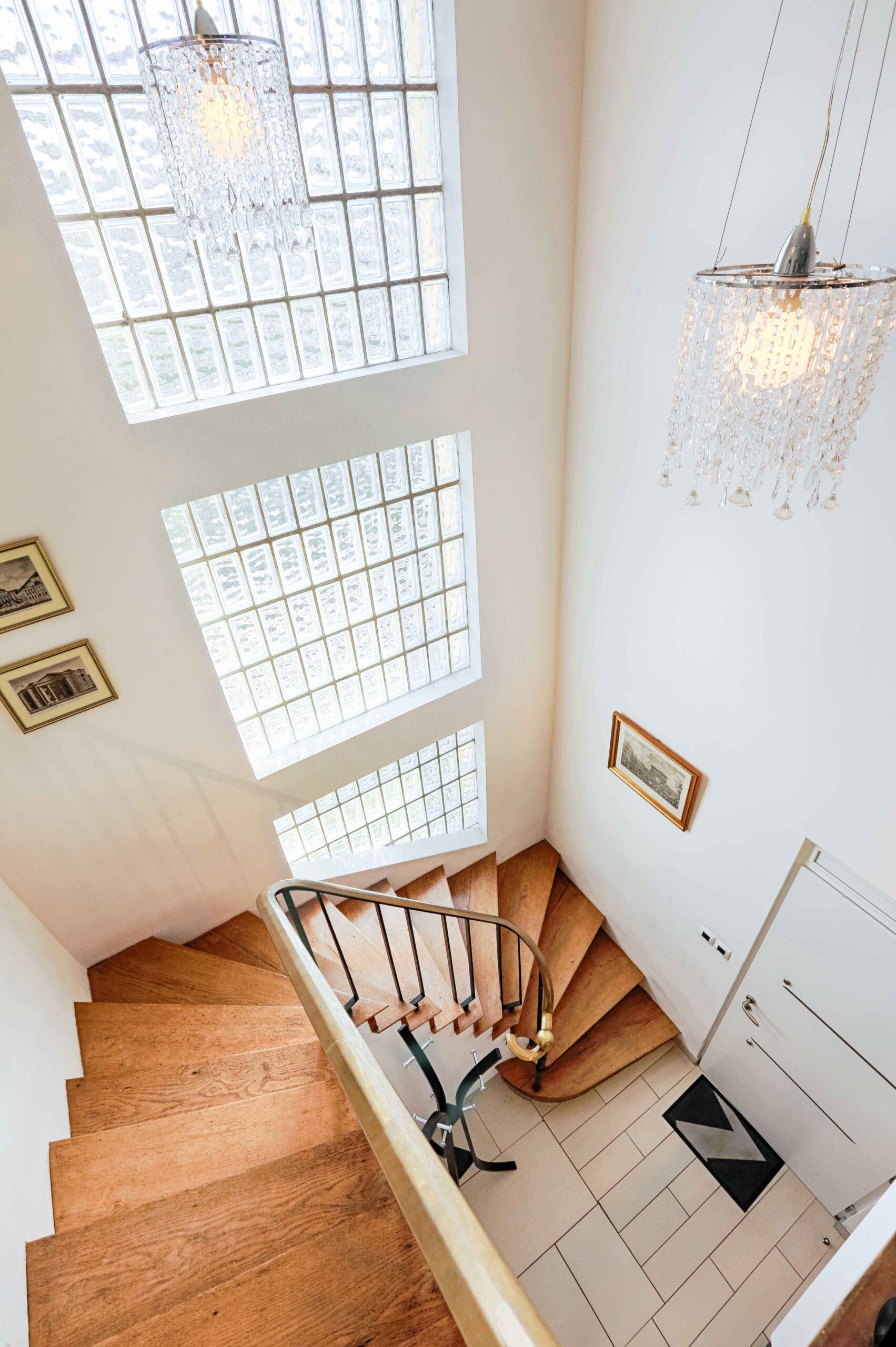 Vue plongeante sur un escalier monumental avec lustres en cristal dans une demeure de luxe.