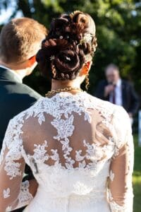 Superbe chignon tressé et dos en dentelle de la robe de mariée lors du vin d'honneur au Moulin de Bully.