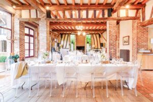Décoration de mariage rustique chic avec longues tables en bois, chemin de table végétal et chaises transparentes.