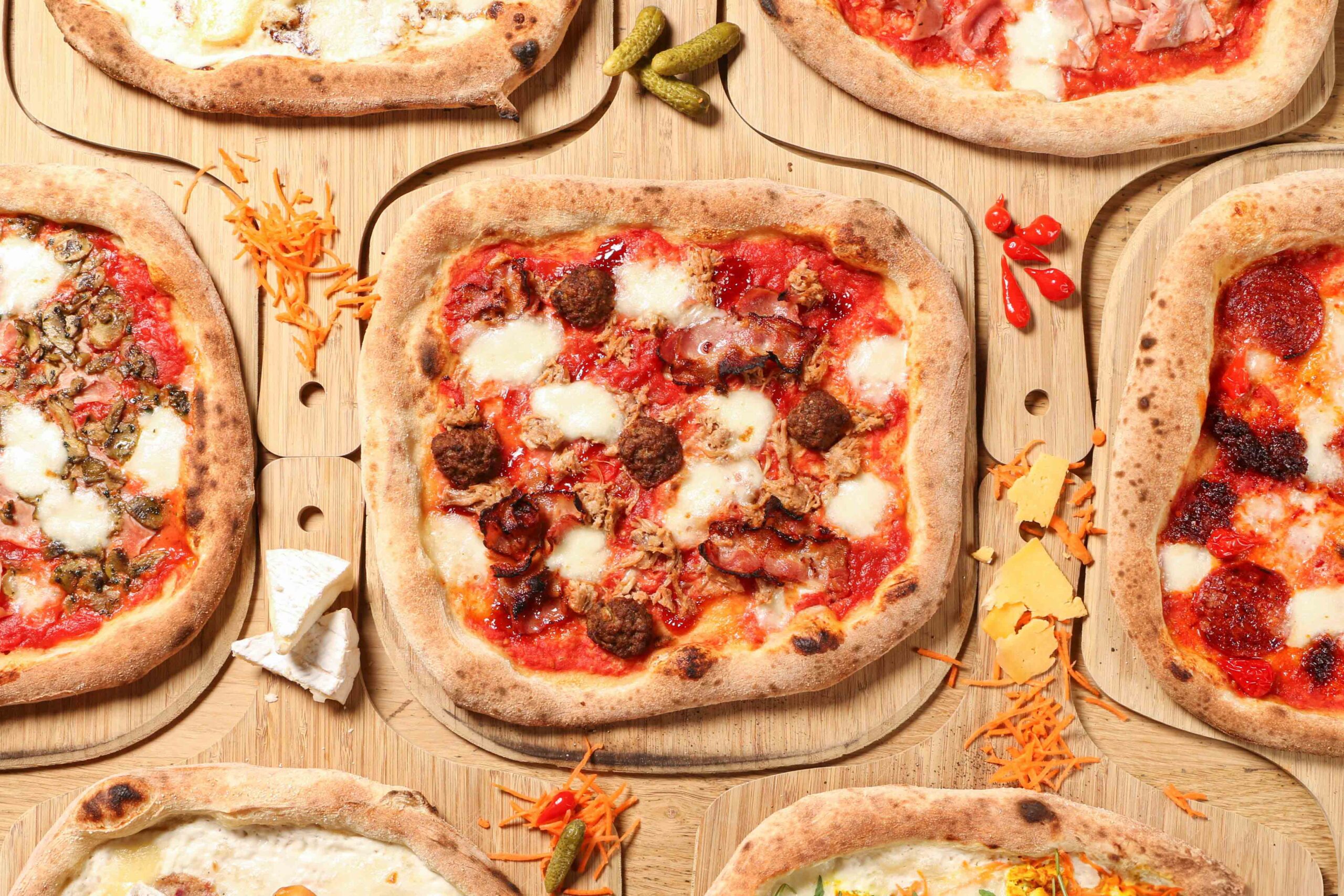 Composition flatlay de pizzas artisanales sur planches en bois avec ingrédients frais.