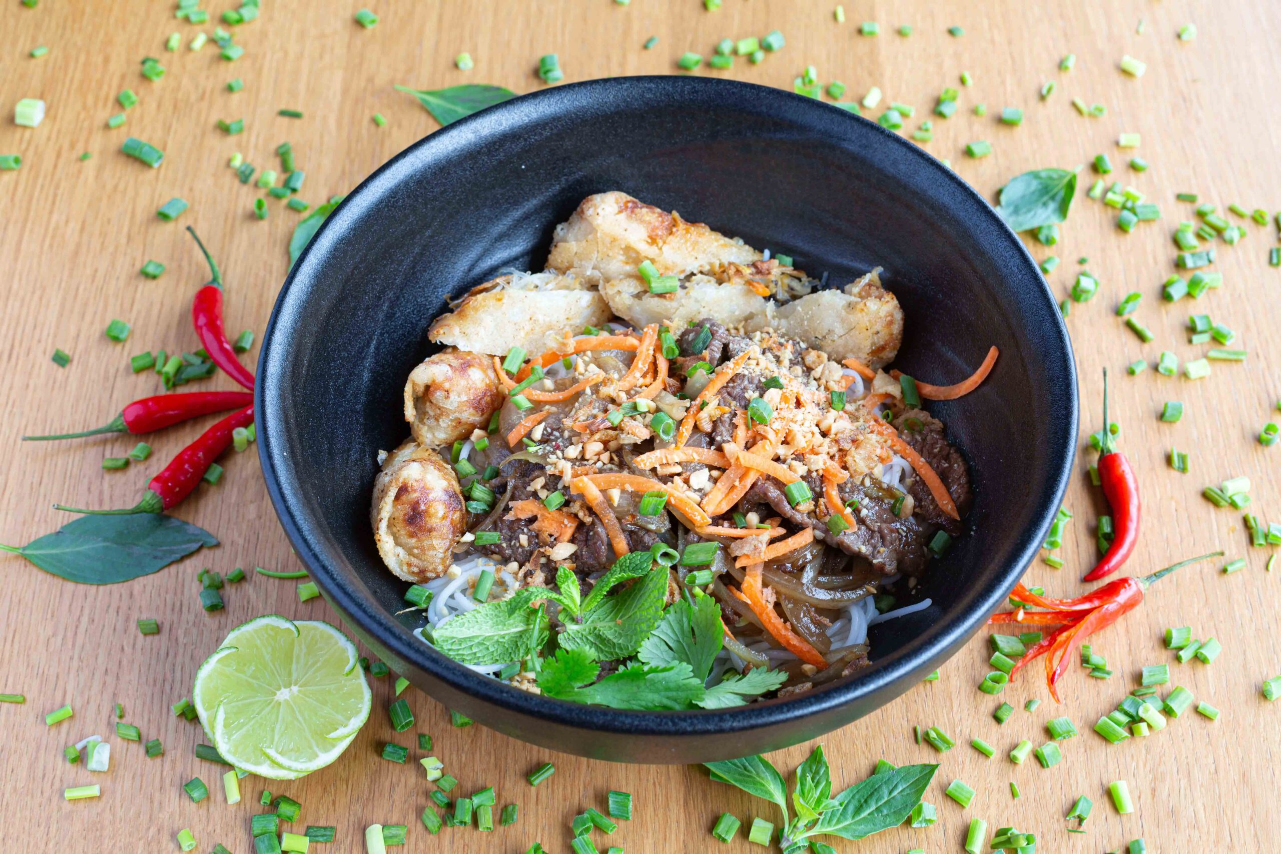 Bol de cuisine asiatique Bun Bo Xao avec nems et herbes fraîches, shooting restaurant.
