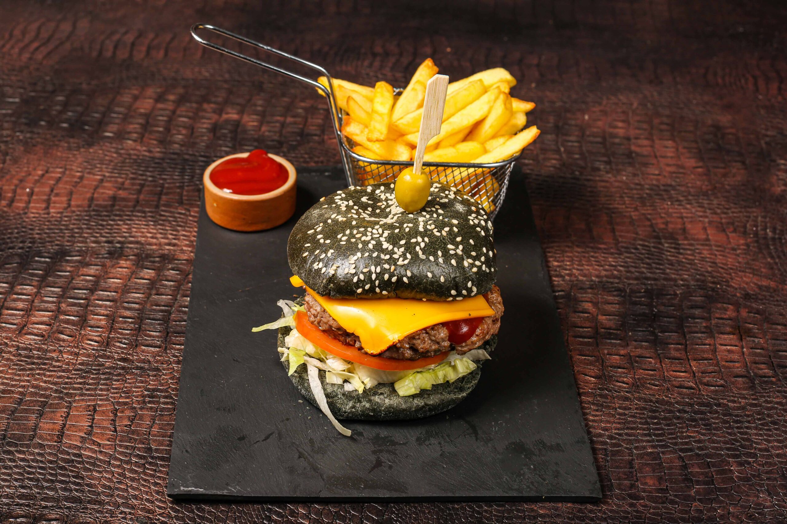 Burger gourmet au pain noir (charbon végétal) servi avec frites croustillantes.