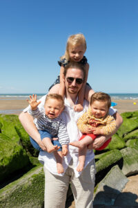 Séance photo famille lifestyle à la plage : un papa s'amuse avec ses trois jeunes enfants près de Deauville.