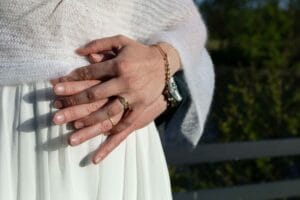 Gros plan sur les mains des mariés entrelacées dévoilant une bague en or avec pierres vertes.