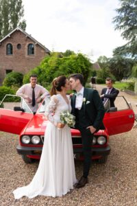 Les mariés s'embrassent devant une voiture de collection rouge vintage lors de leur mariage à Deauville.