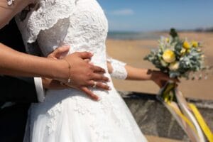 Détail de la robe de mariée en dentelle et du bouquet de fleurs fraîches lors de la séance couple à Trouville.