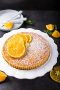 Gâteau à l'orange et sucre glace présenté sur un plat de service vintage blanc.