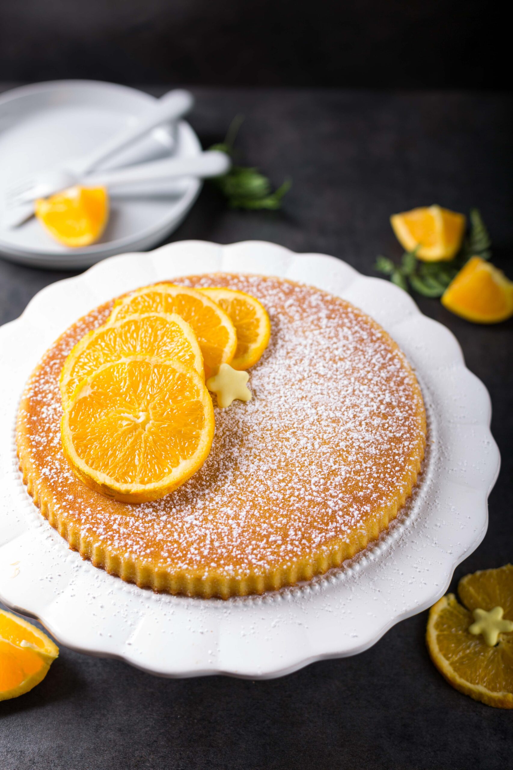 Gâteau à l'orange et sucre glace présenté sur un plat de service vintage blanc.