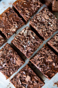 Détail de carrés de brownie au chocolat noir saupoudrés de copeaux de cacao.