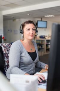 Collaboratrice en centre d'appels souriante avec casque audio lors d'un shooting corporate.