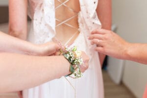 Les témoins aident la mariée à enfiler et boutonner sa robe de mariée dos nu en dentelle.