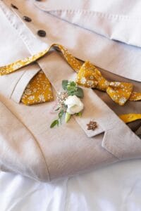 Costume de marié beige en lin, accompagné d'un nœud papillon à fleurs jaunes et de sa boutonnière.