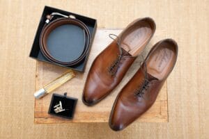 Accessoires du marié : chaussures en cuir marron, montre classique et parfum avant la cérémonie.