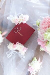 Alliances de mariage dans leur célèbre écrin rouge Cartier entourées de fleurs fraîches pastel.