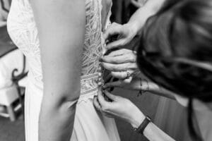 Les demoiselles d'honneur aident la mariée à boutonner sa robe de mariée en dentelle.