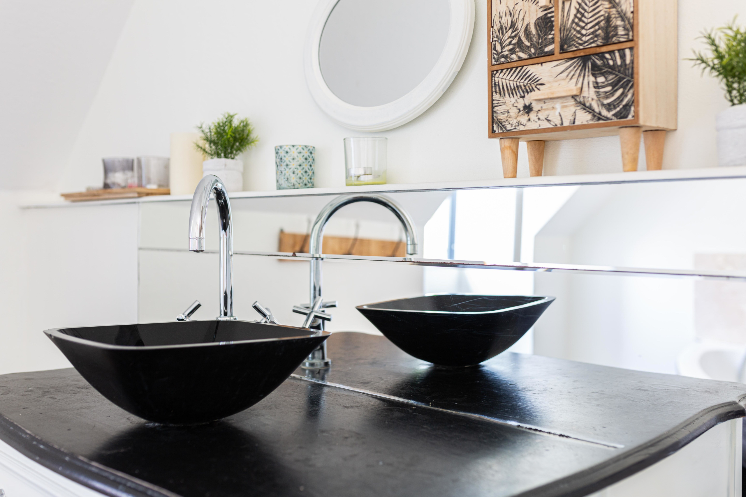 Détail d'une salle de bain moderne avec vasque noire et grand miroir.