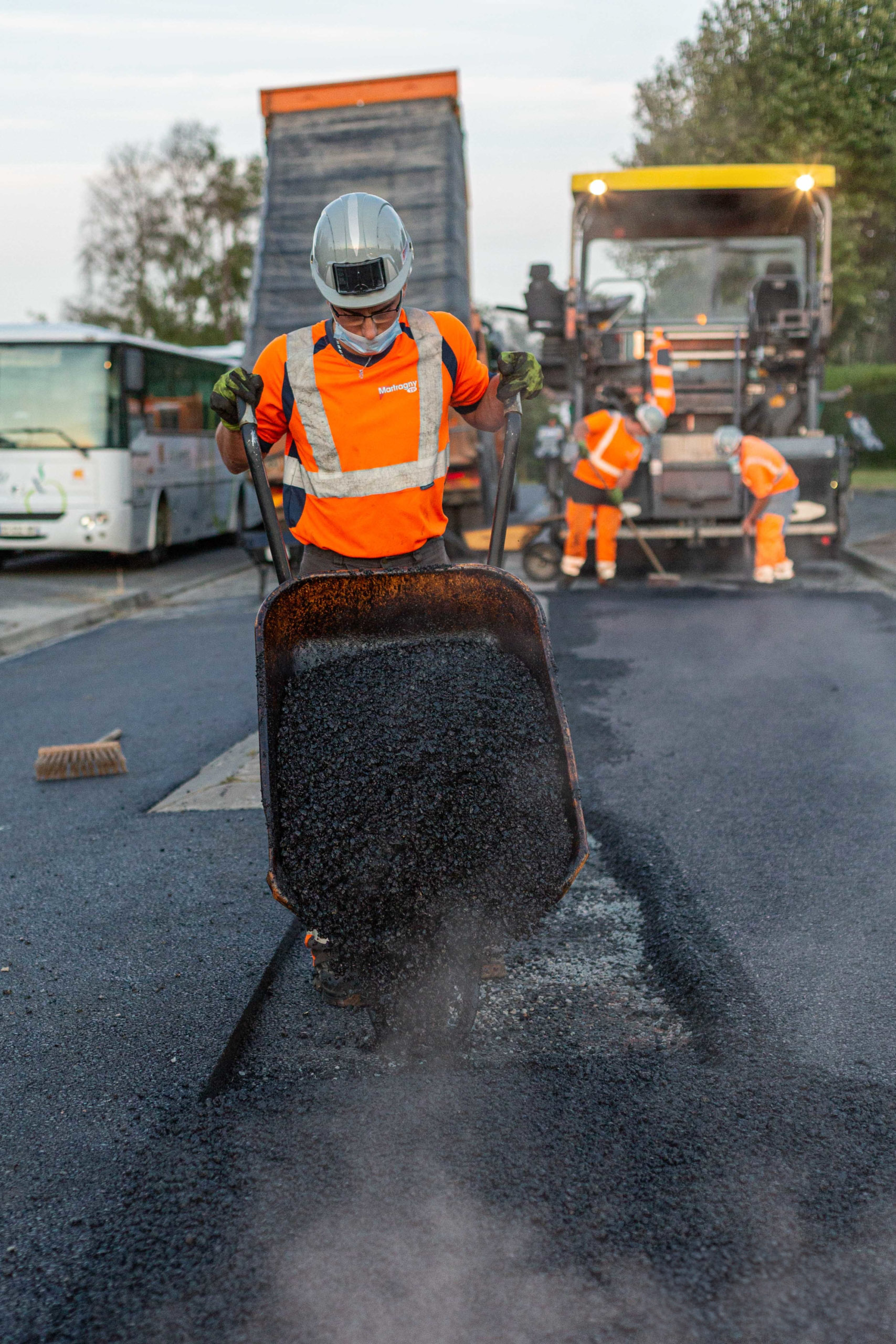 Gros plan technique sur l'application d'un enrobé bitumineux lors de travaux routiers au coucher du soleil.