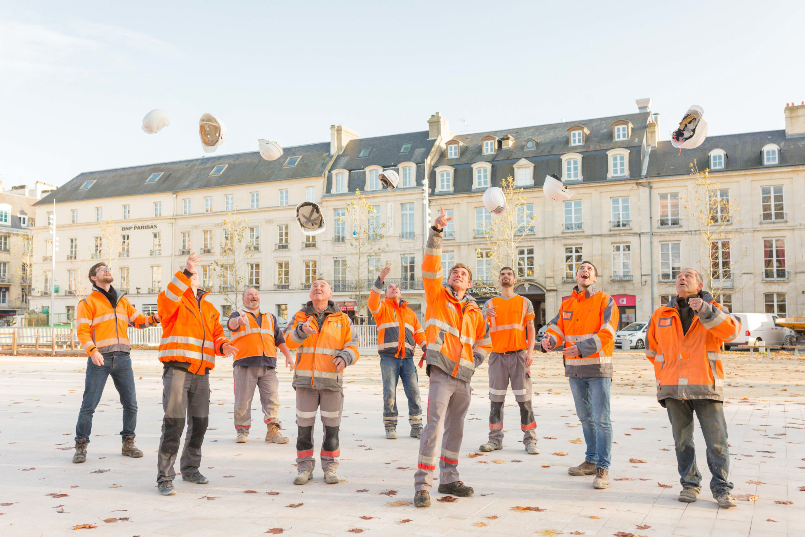 Ouvriers du bâtiment lançant leurs casques sur un chantier à Caen pour une photo d'équipe.