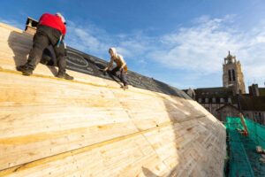Compagnon couvreur travaillant sur une toiture avec vue sur les clochers de Caen.