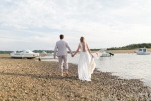 Promenade romantique des mariés sur le sable à marée basse avec les bateaux en arrière-plan.