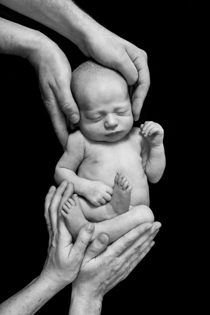 Photo de naissance symbolique en noir et blanc montrant le bébé protégé par les mains de ses parents.