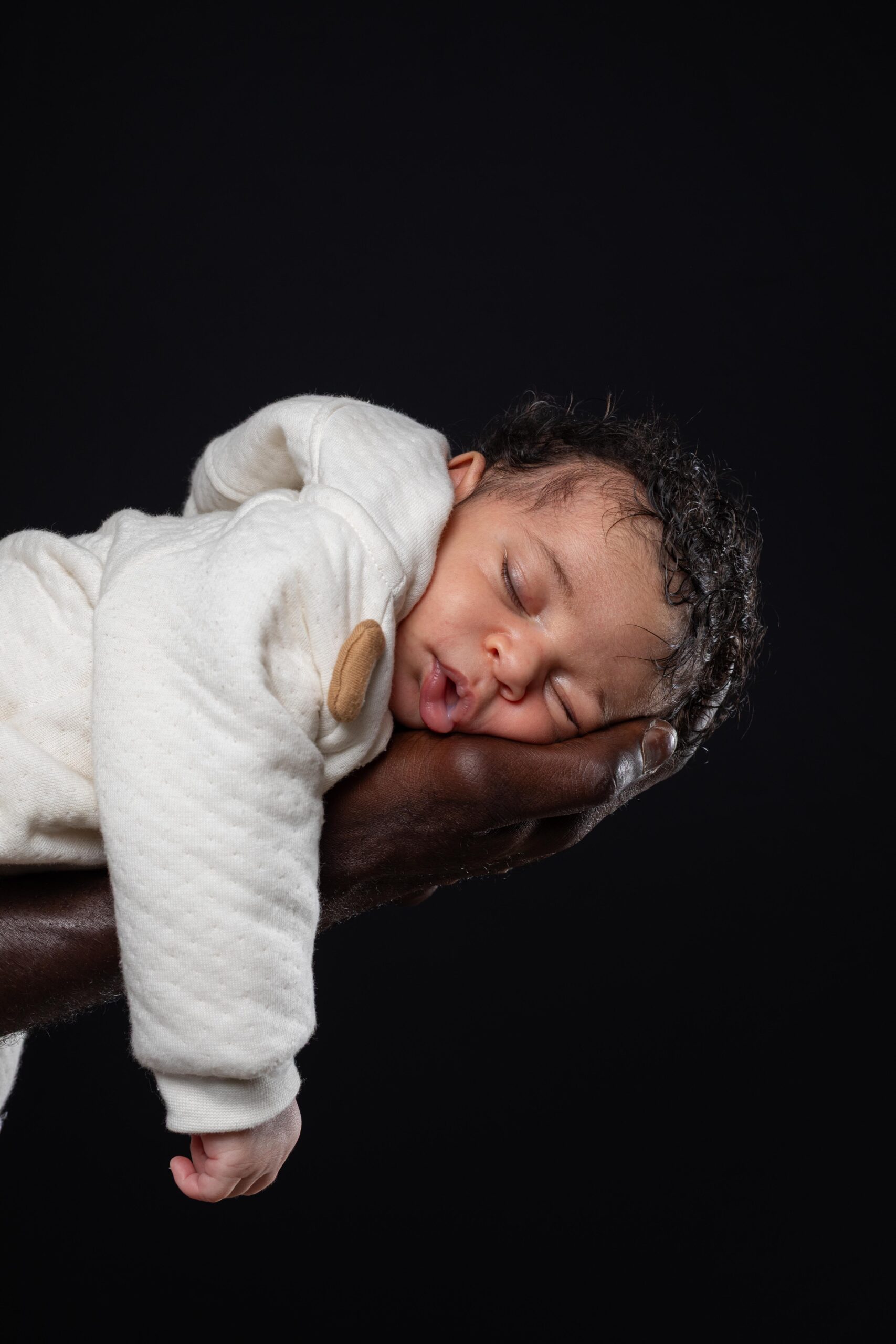 Détail touchant d'un bébé dormant paisiblement sur la main de son père, photographe Deauville.