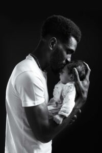 Photographie en noir et blanc d'un père embrassant son nouveau-né, studio photo Honfleur
