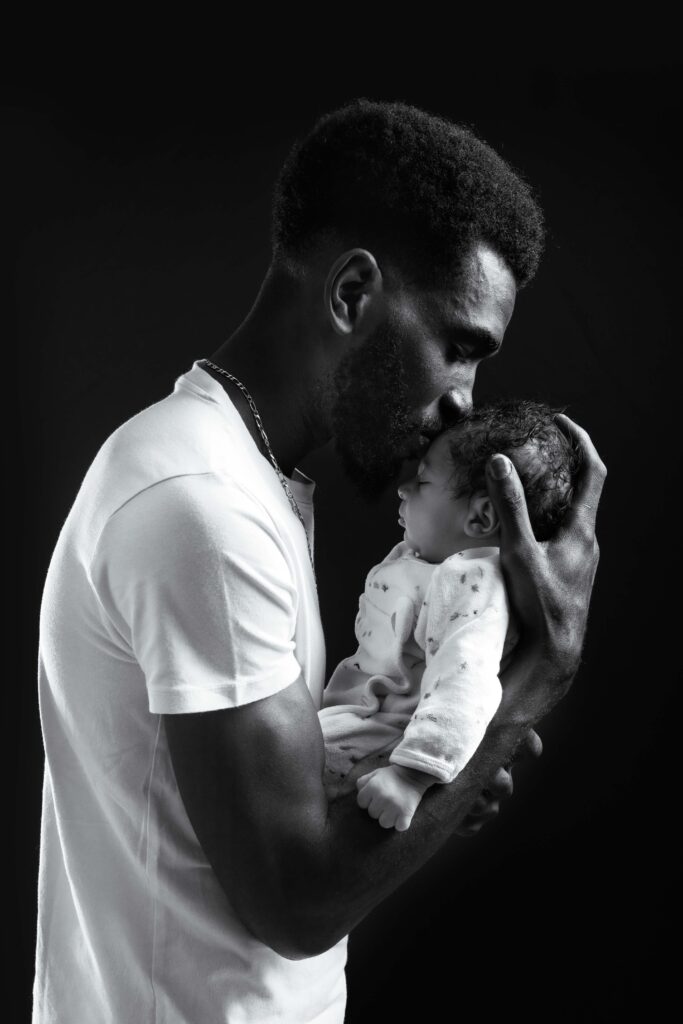 Photographie en noir et blanc d'un père embrassant son nouveau-né, studio photo Honfleur