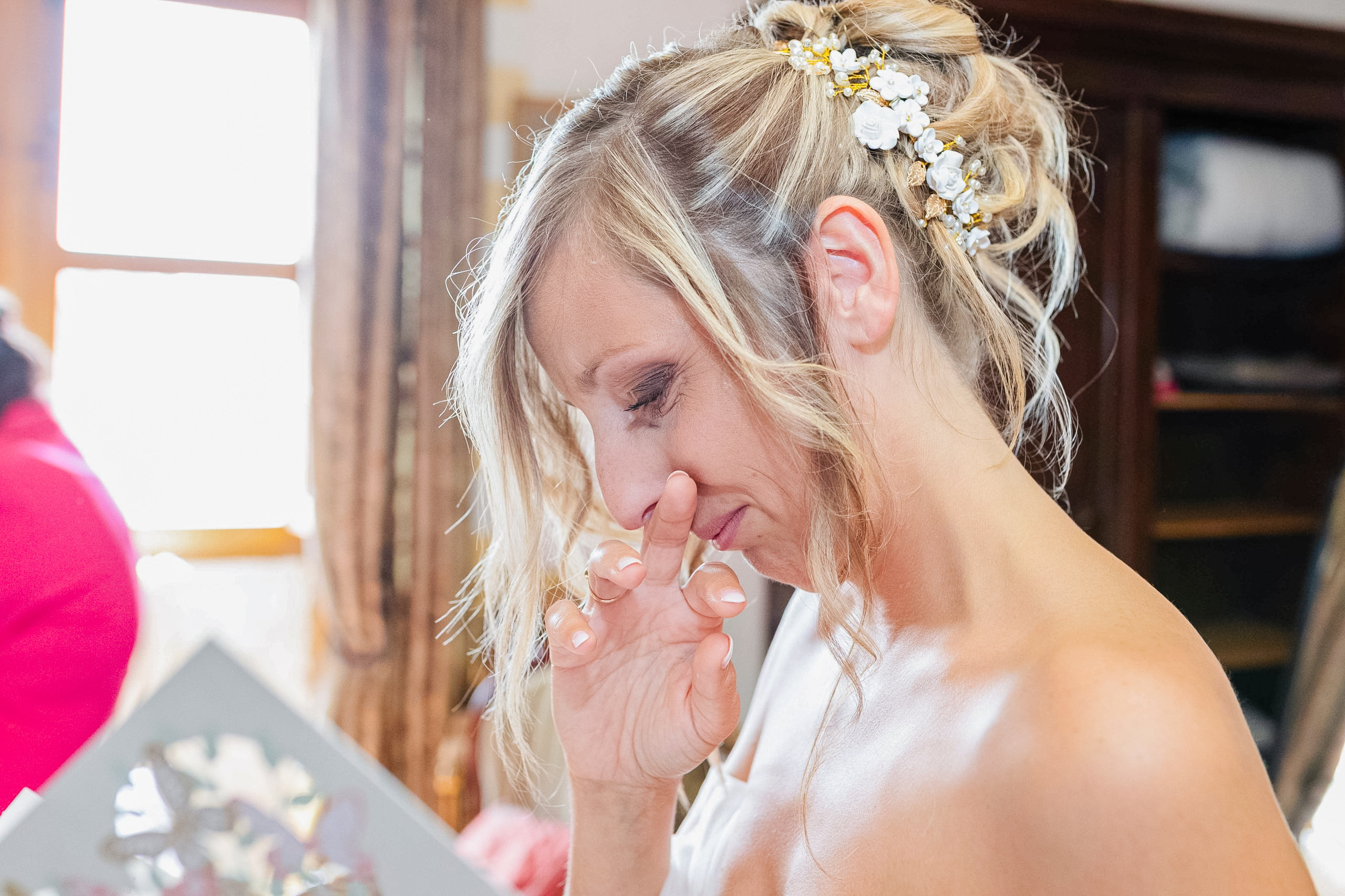 Gros plan sur le profil de la mariée essuyant délicatement une larme d'émotion, mettant en valeur son accessoire de coiffure fleuri.