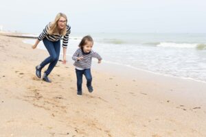 Une femme et une petite fille courant joyeusement sur une plage de sable fin, toutes deux portant des marinières assorties.