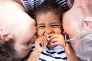 Une petite fille comblée de bonheur recevant un bisou affectueux de chaque côté de la part de ses proches.