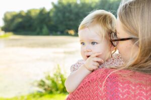 Une maman portant son jeune enfant sur l'épaule, regardant ensemble vers l'horizon dans un parc ensoleillé.