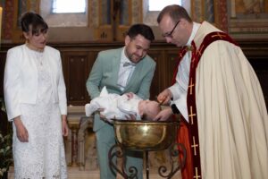 Un prêtre verse de l'eau bénite sur la tête d'un bébé lors d'un baptême à l'église, entouré de ses parents émus.