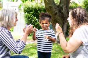 Une petite fille et deux femmes s'amusant à faire des bulles de savon dans un jardin verdoyant en été.