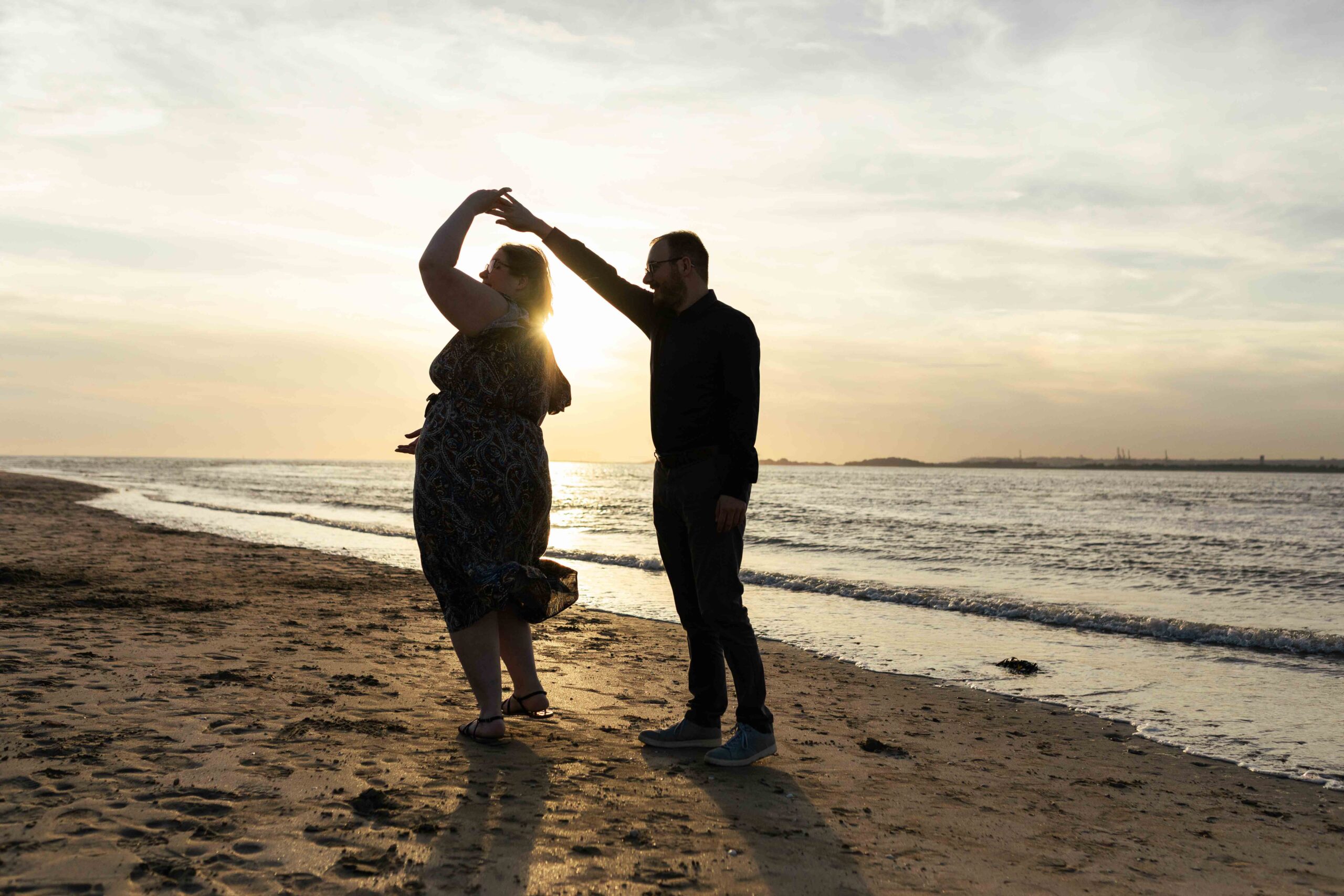 Couple d'amoureux dansant sur la plage au coucher du soleil lors d'une séance photo romantique près de Deauville.