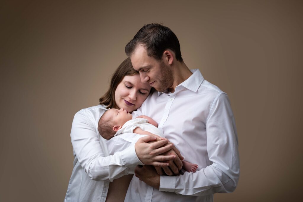 Séance photo famille au studio de Honfleur : de jeunes parents complices admirent leur nouveau-né, près de Lisieux.