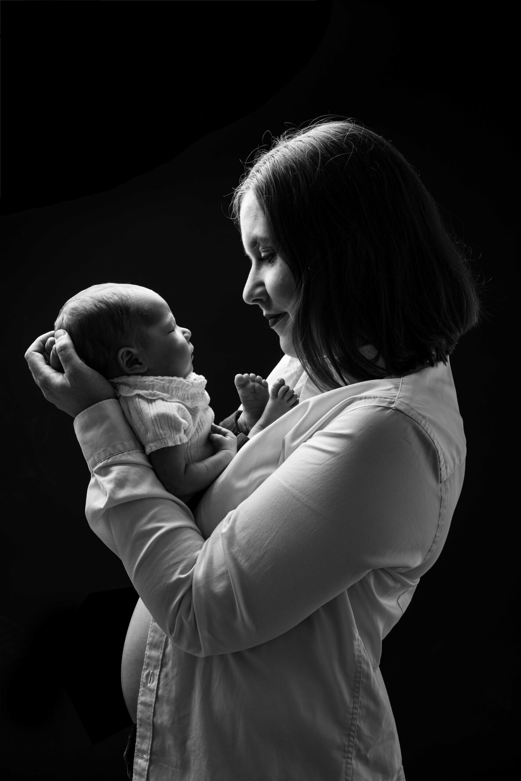 Shooting naissance en clair-obscur : une maman regarde son bébé avec amour en noir et blanc, studio photo près de Pont-Audemer.