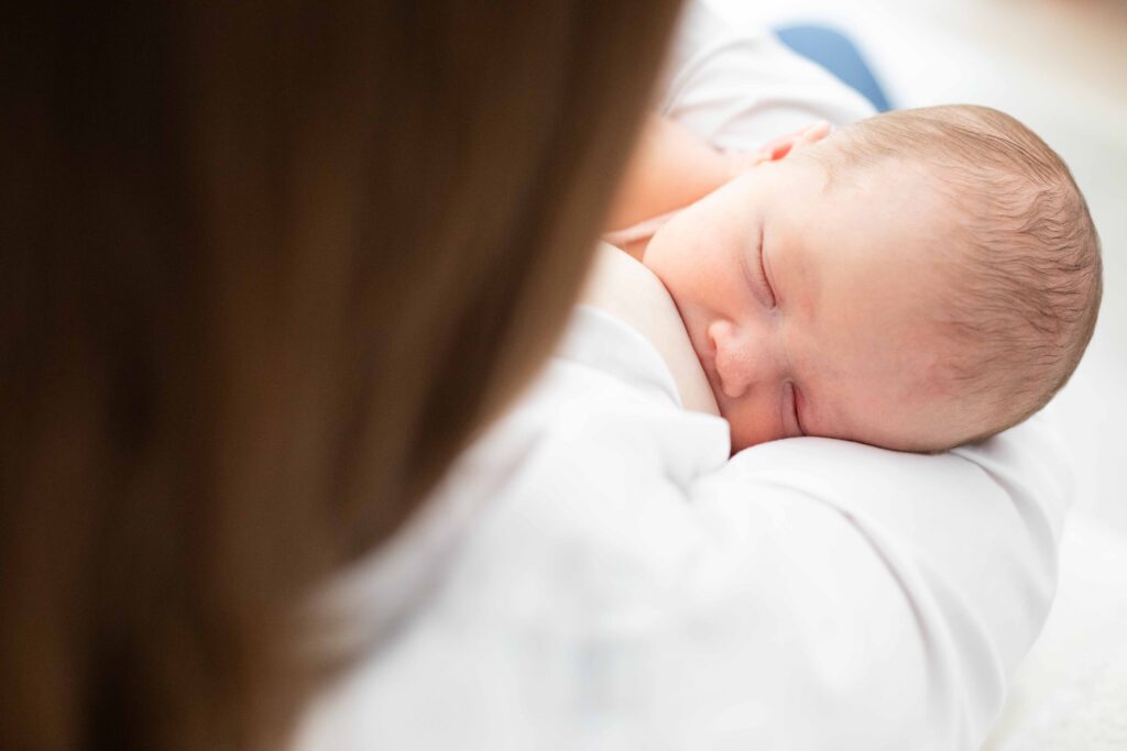 Instant de douceur et d'intimité capturé lors d'une séance photo de naissance : maman allaitant son bébé en Normandie.