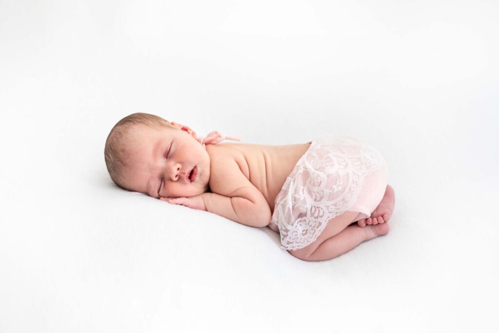 Nouveau-né endormi paisiblement sur fond blanc avec une délicate culotte en dentelle, séance photo bébé près de Caen.