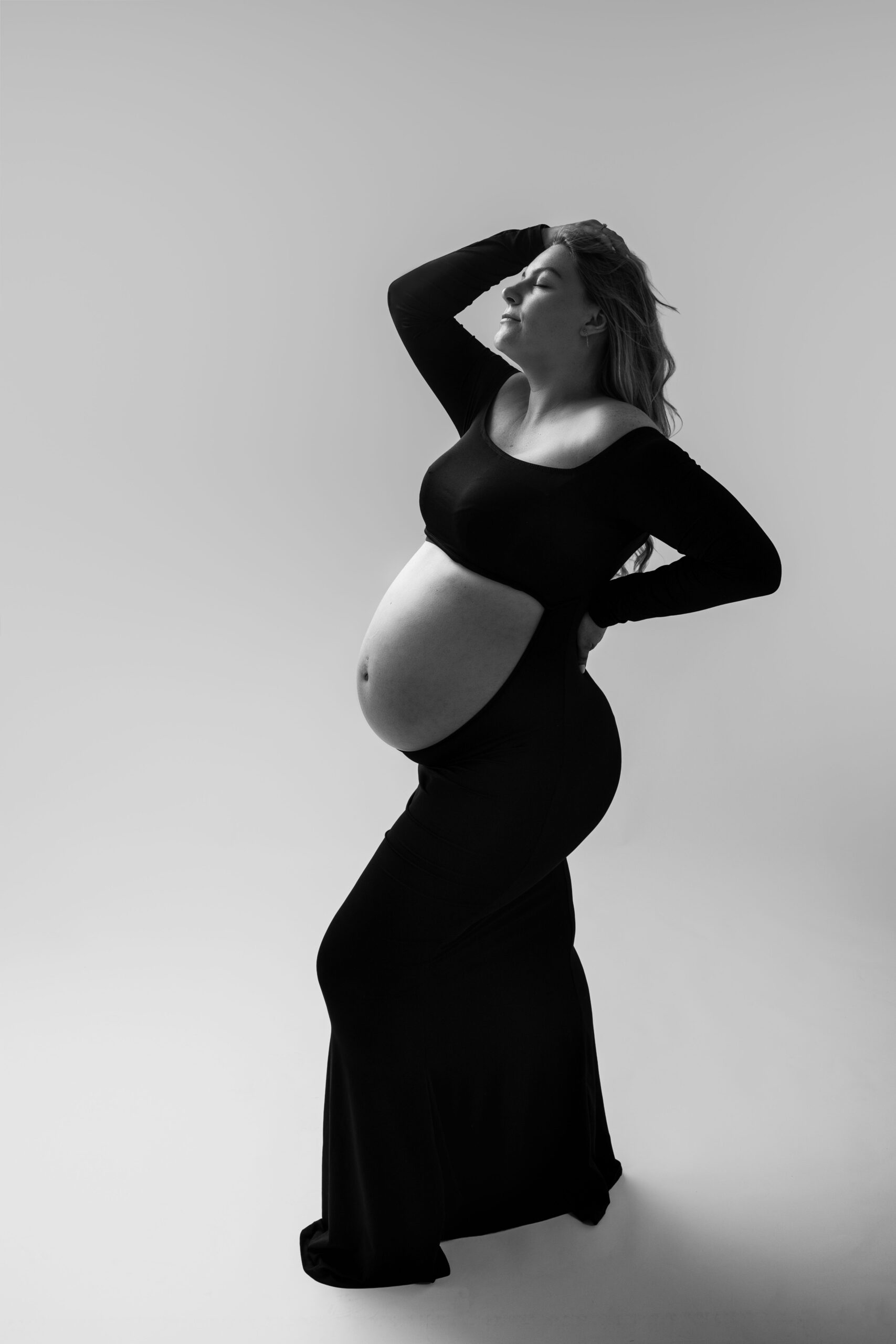 Photographe maternité près de Deauville : portrait artistique en noir et blanc d'une femme enceinte posant en robe noire.
