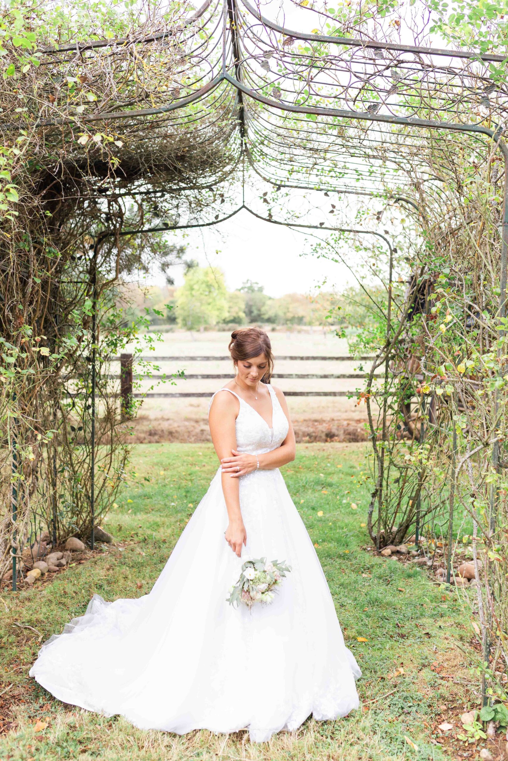 Portrait de la mariée souriante avec son bouquet sous une arche végétale, shooting de mariage au Havre.