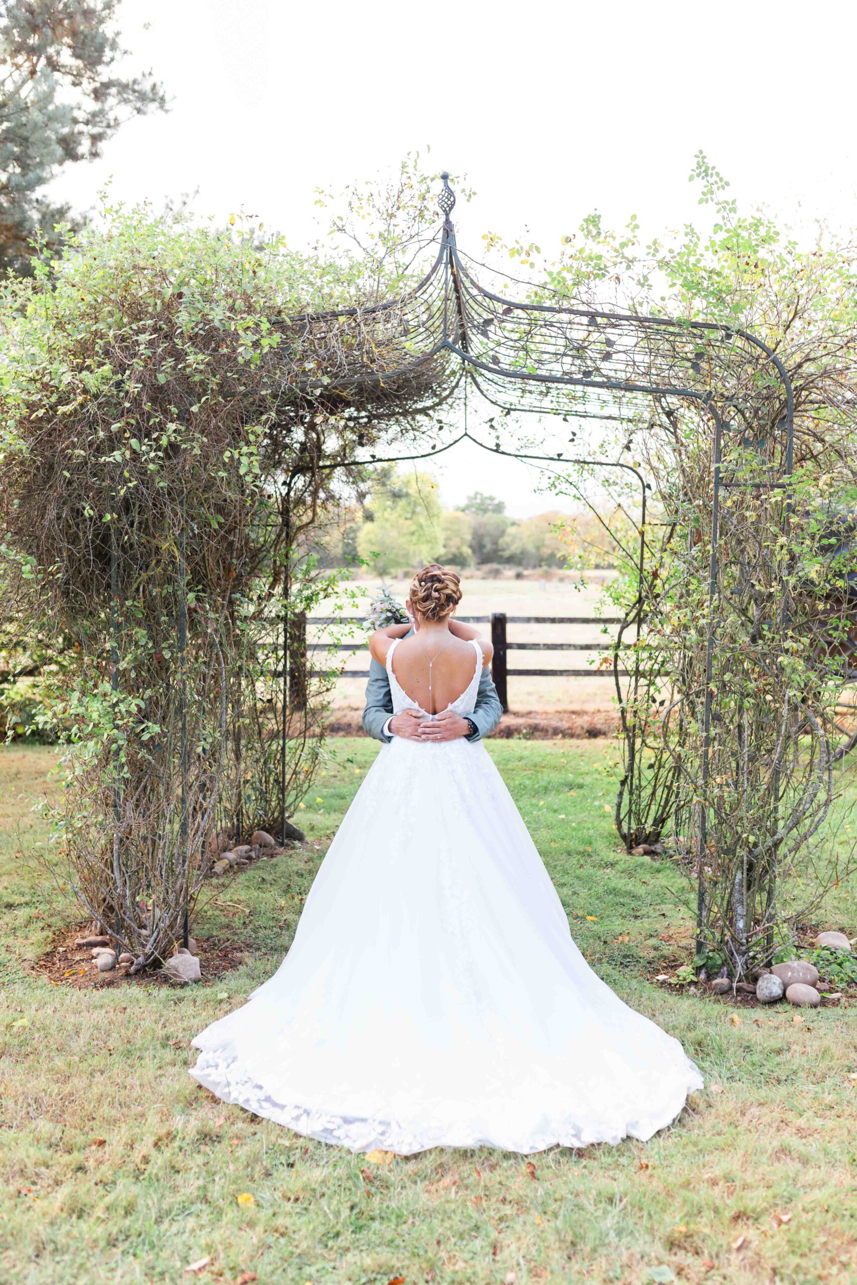 La mariée de dos montre le magnifique décolleté de sa robe sous une arche en fer forgé au domaine de la tour.